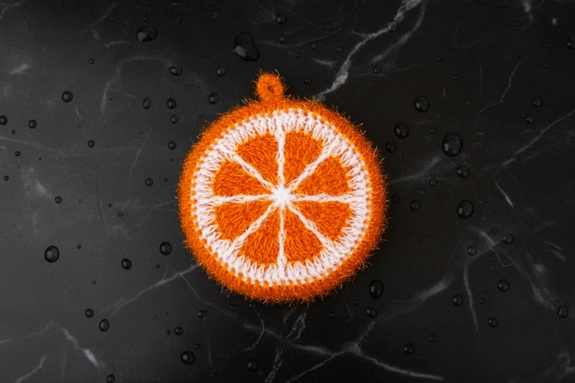Deep orange-colored hand-crocheted dish scrubber on a wet matte black marble stone surface.