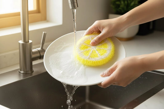 Person washing a plate with a yellow lemon dish scrubber in a kitchen sink.