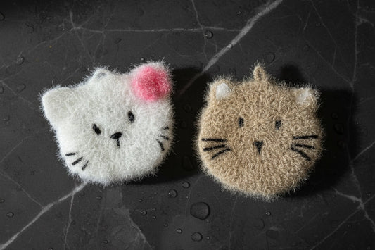 Two cat-shaped crocheted dish scrubbers on a dark textured surface