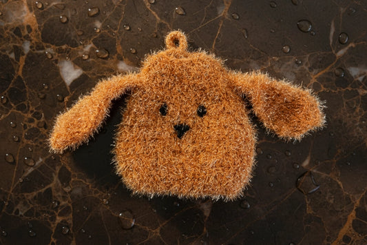 Brown dog-shaped dish scrubber on a dark marble surface