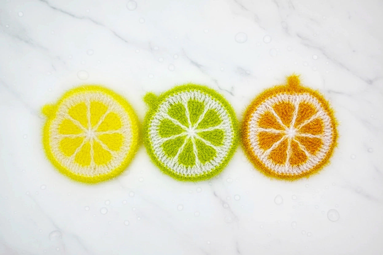 Three crocheted dish scrubbers: lemon, lime, and orange slices on a white background