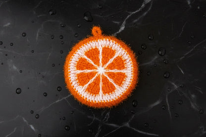 Deep orange-colored hand-crocheted dish scrubber on a wet matte black marble stone surface.