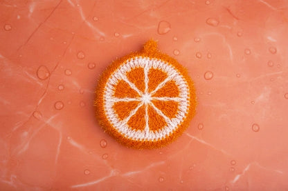 Cara cara citrus squeeze scrubbie — Deep orange-colored hand-crocheted dish scrubber on a we orange marble stone surface.