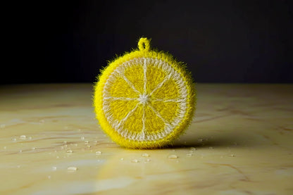 Yellow lemon-shaped dish scrubber on a textured stone surface with a dark background