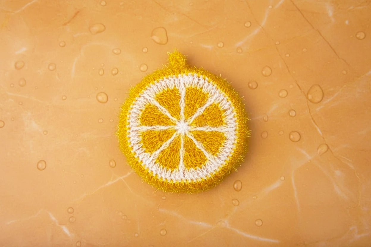 Crocheted orange slice dish scrubber on a textured orange background