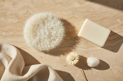 Bar of soap, loofah, and an ivory scrubby on a beige surface.