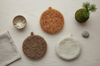 Designer Series: Mocha Collection Hello Scrubbies in chocolate brown, caramel, and ivory on a light wooden surface with a towel and small plant.