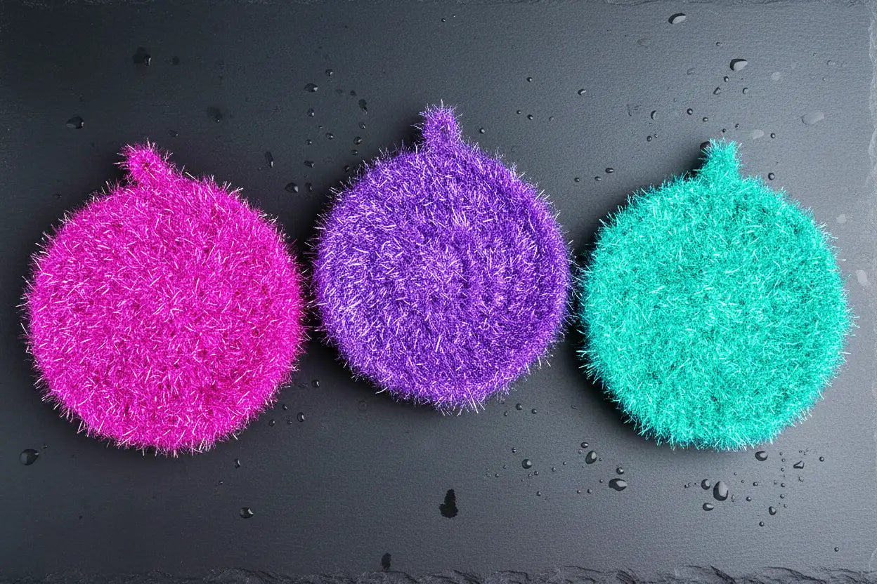 Trio of colorful Neon Collection scrubbies (magenta, purple, turquoise) on a dark surface with water droplets.