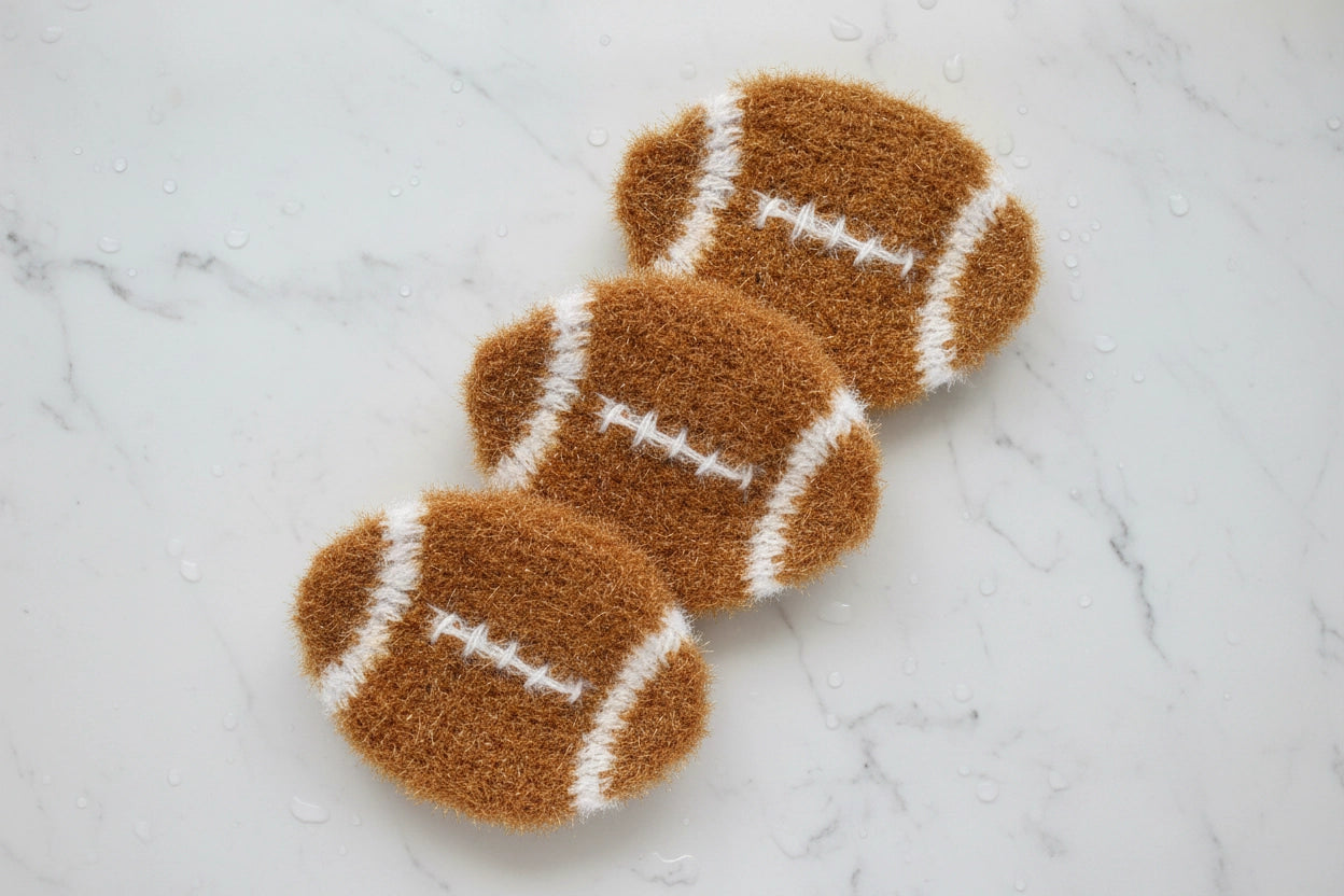 Three brown and white football-shaped dish scrubbers on a marble surface
