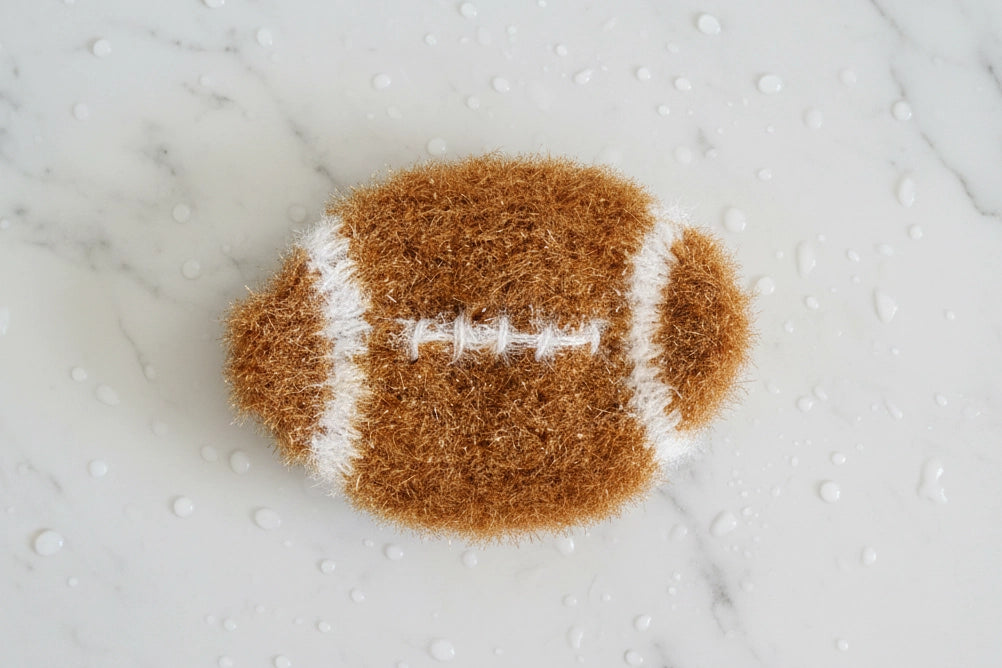 Football-shaped dish scrubber on a textured white surface