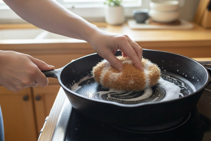 Person scrubbing a cast iron pan on a stove with a football-shaped dish scrubber.