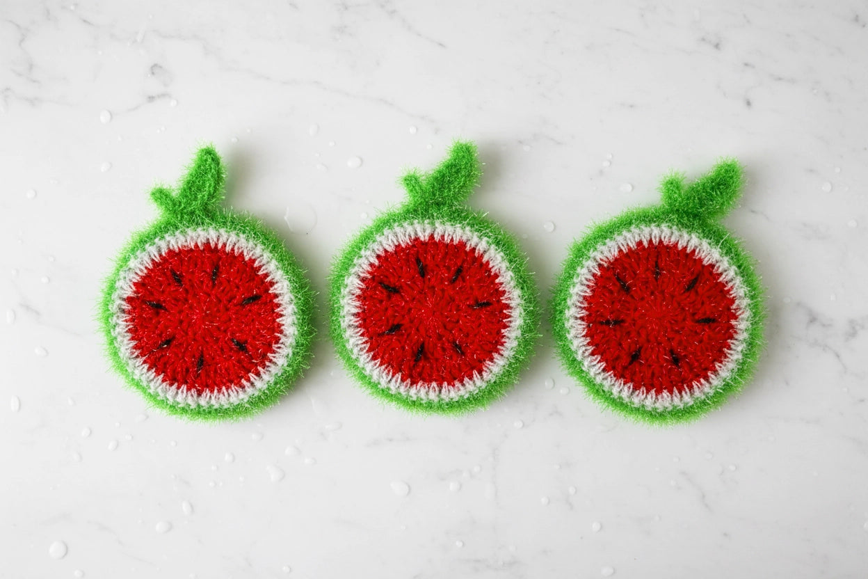 Three crocheted watermelon dish scrubbers on a white marble surface