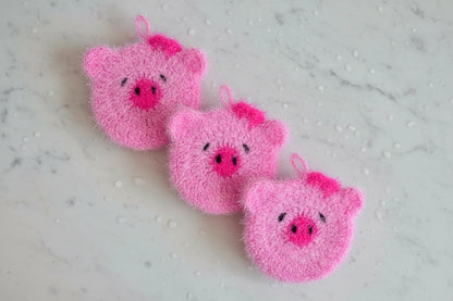Three pink pig-shaped dish scrubber on a marble surface