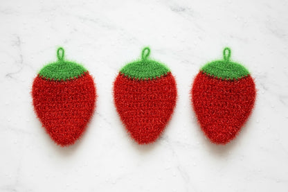Three red strawberry-shaped dish scrubbers with green tops on a white background