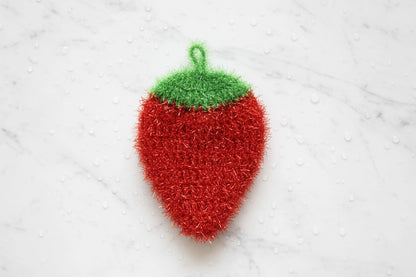 Red strawberry-shaped dish scrubber with a green top on a white textured background