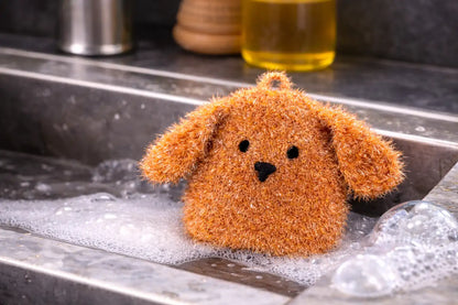 Brown dog-shaped dish scrubber on a kitchen sink with soapy water