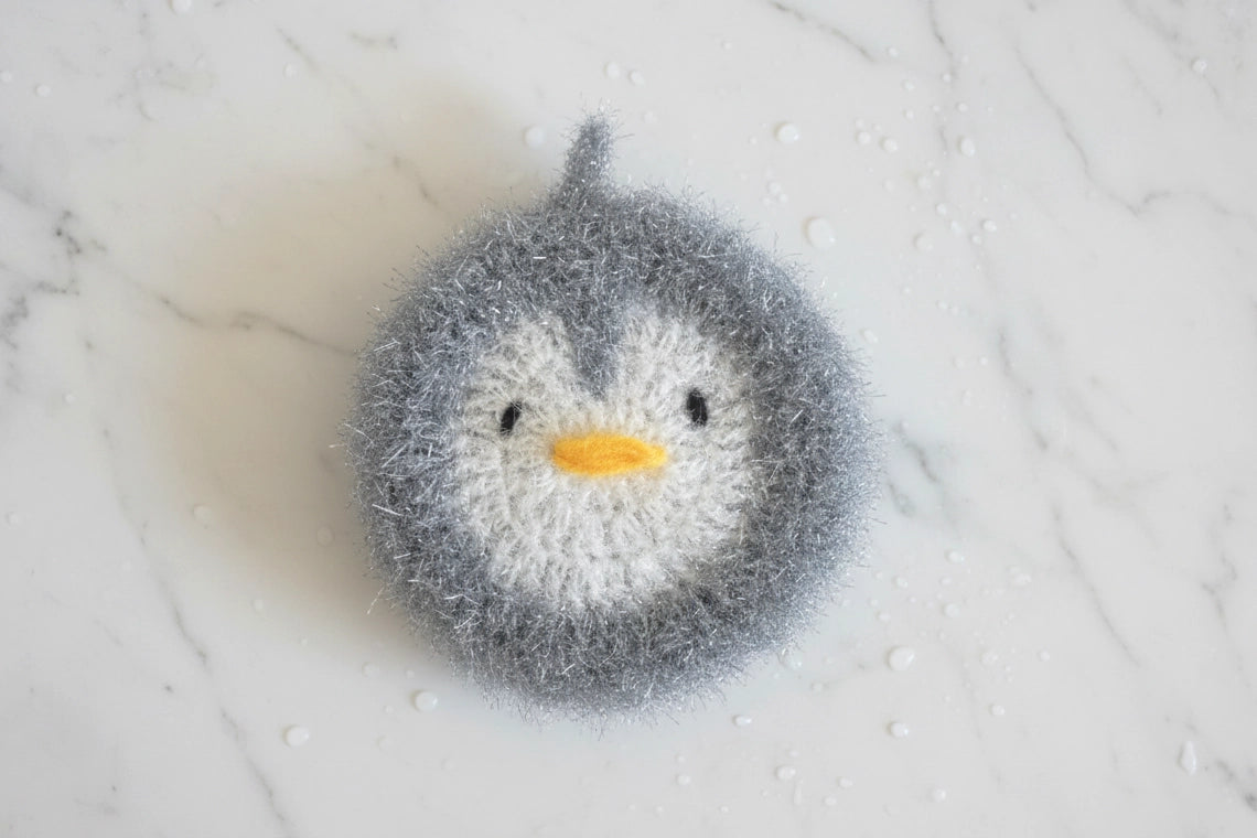 Gray penguin-shaped dish scrubber on a white marble surface