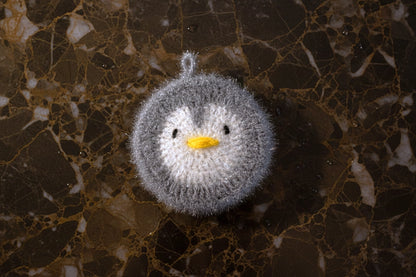 Crocheted gray penguin dish scrubber on a marble surface
