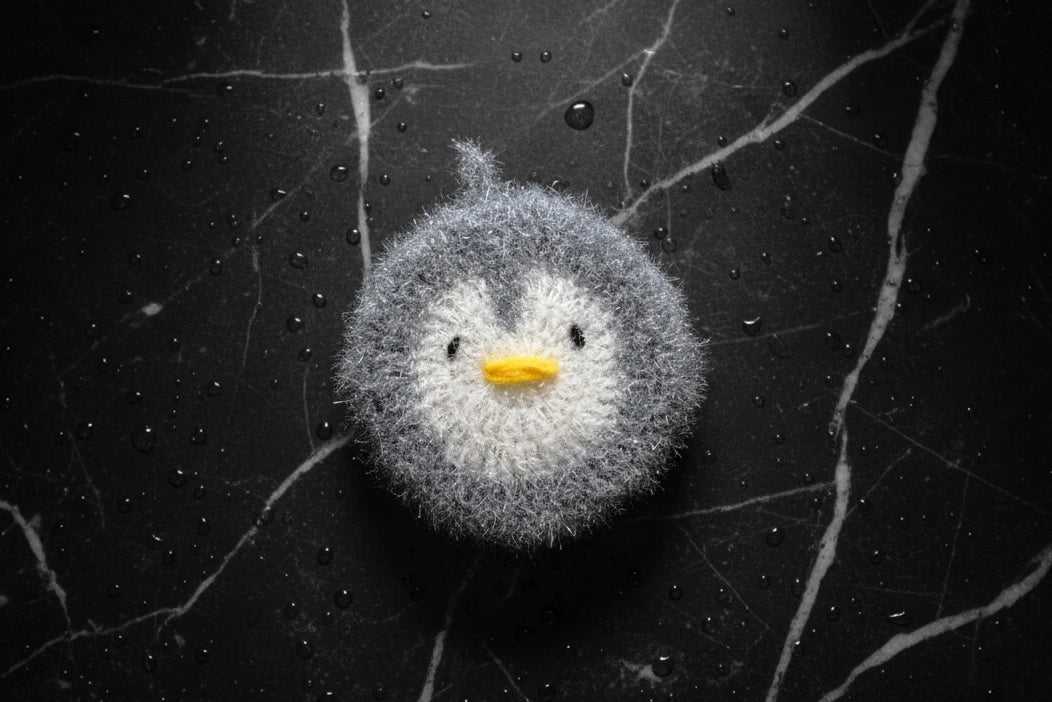 Gray penguin-shaped dish scrubber on a textured black surface