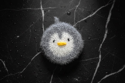 Gray penguin-shaped dish scrubber on a textured black surface