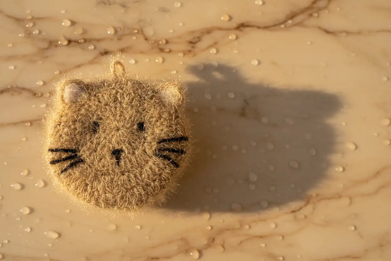 Textured hand-crocheted dish scrubber with a cat face on a marble surface