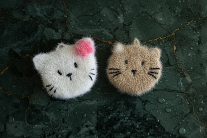 Two fluffy cat-shaped dish scrubbers on a dark textured surface