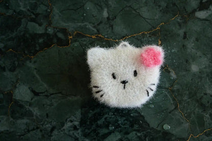 White cat-shaped dish scrubber with a pink flower on a dark textured surface
