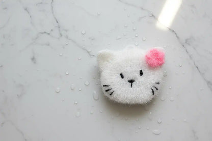 White cat-shaped dish scrubber with a pink flower on a marble surface