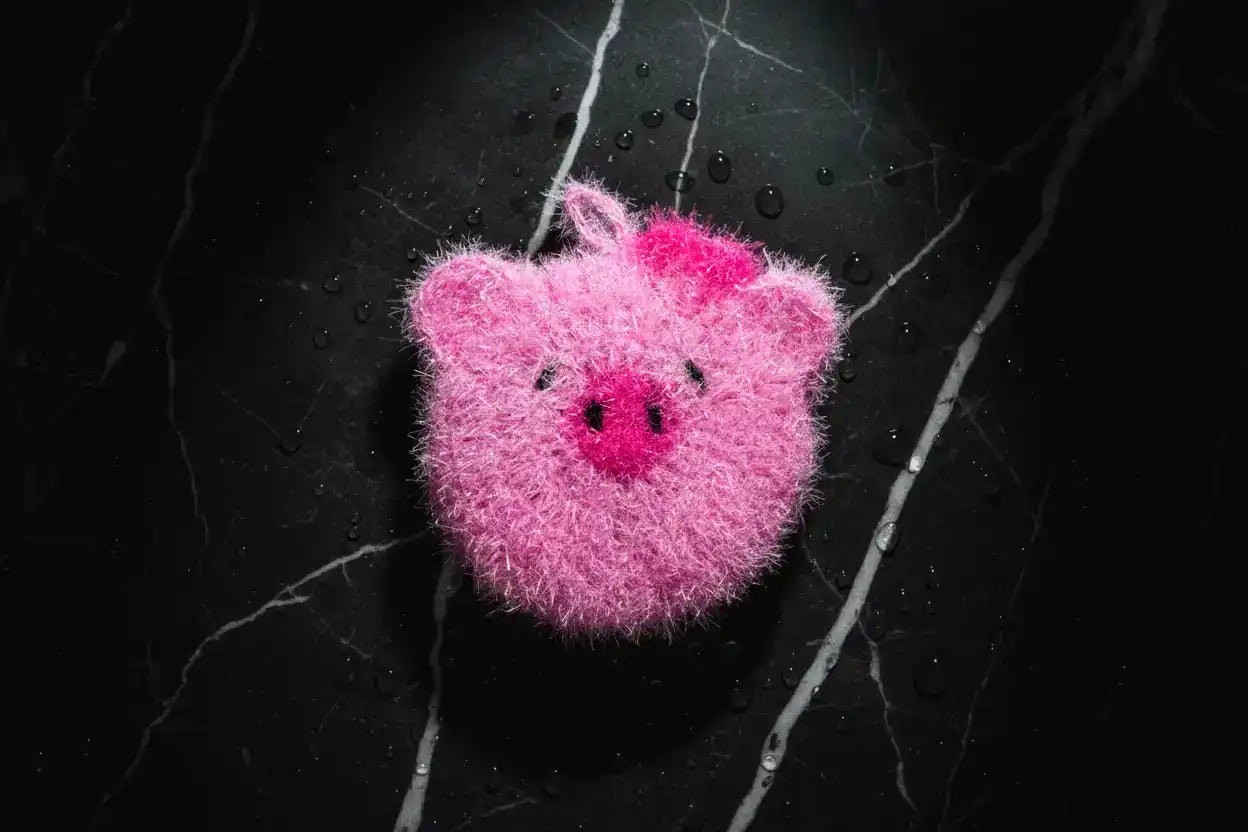Pink pig dish scrubber on a black textured background