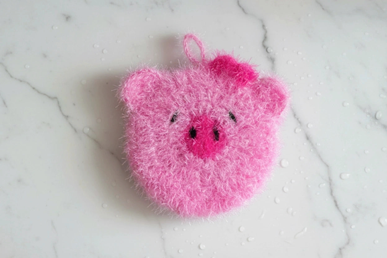 Cute pink pig dish scrubber on a white marble surface