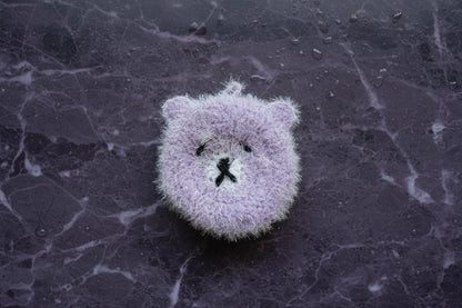 Fuzzy purple bear dish scrubber on a textured dark surface