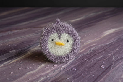 Purple crocheted penguin-shaped dish scrubber on a marbled surface