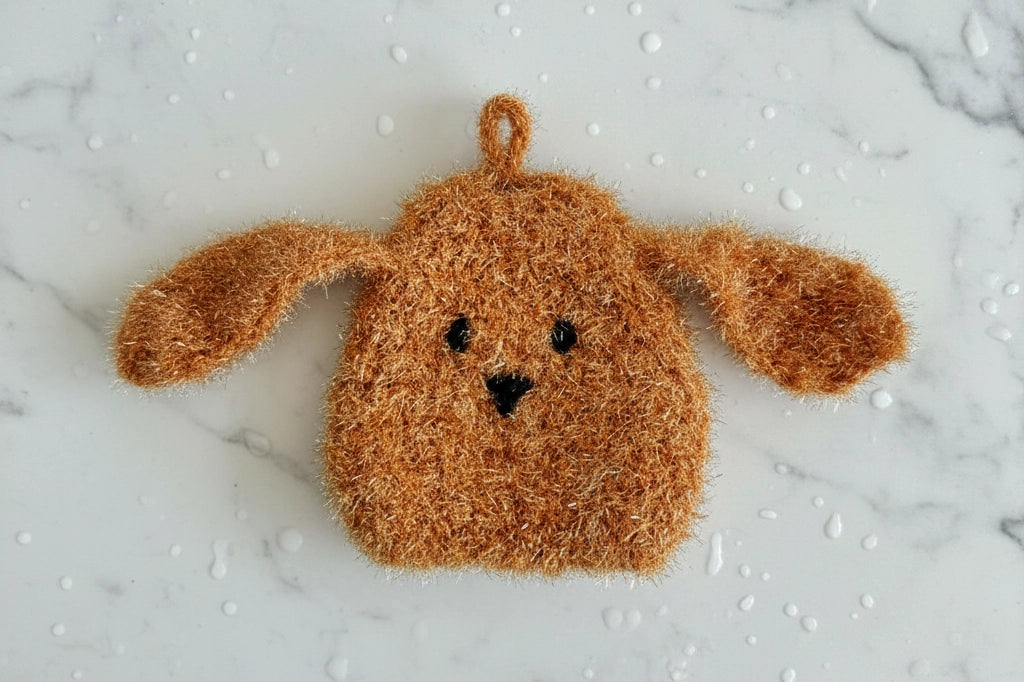 Rufus — brown long-eared fuzzy dog dish scrubber on a white marble surface