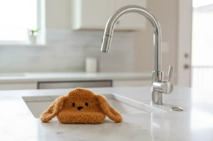 Brown doggy dish scrubber with floppy long ears on a kitchen sink with a modern faucet.