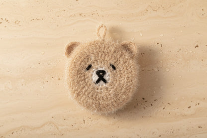 Small light brown bear-shaped dish scrubber on a textured travertine surface
