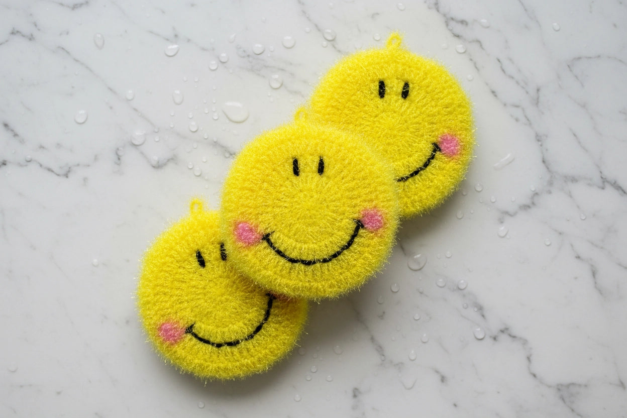 Three yellow smiley face dish scrubbers on a marble surface