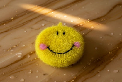 Yellow smiley face dish scrubber on a textured beige surface