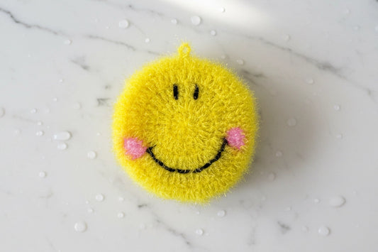 Yellow smiley face dish scrubber on a marble surface with water droplets.